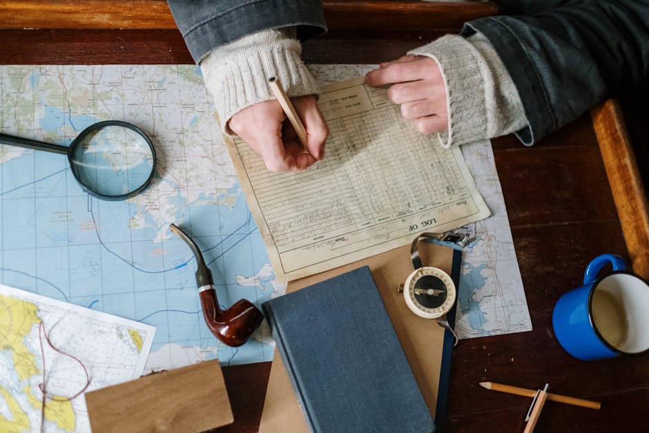 Top view of hand writing on logbook with map, compass, and pipe.