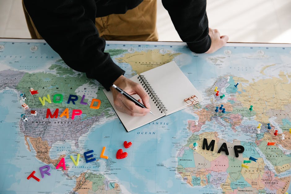 A person writing in a notebook on a world map, planning a travel journey with colorful markers and a pen.