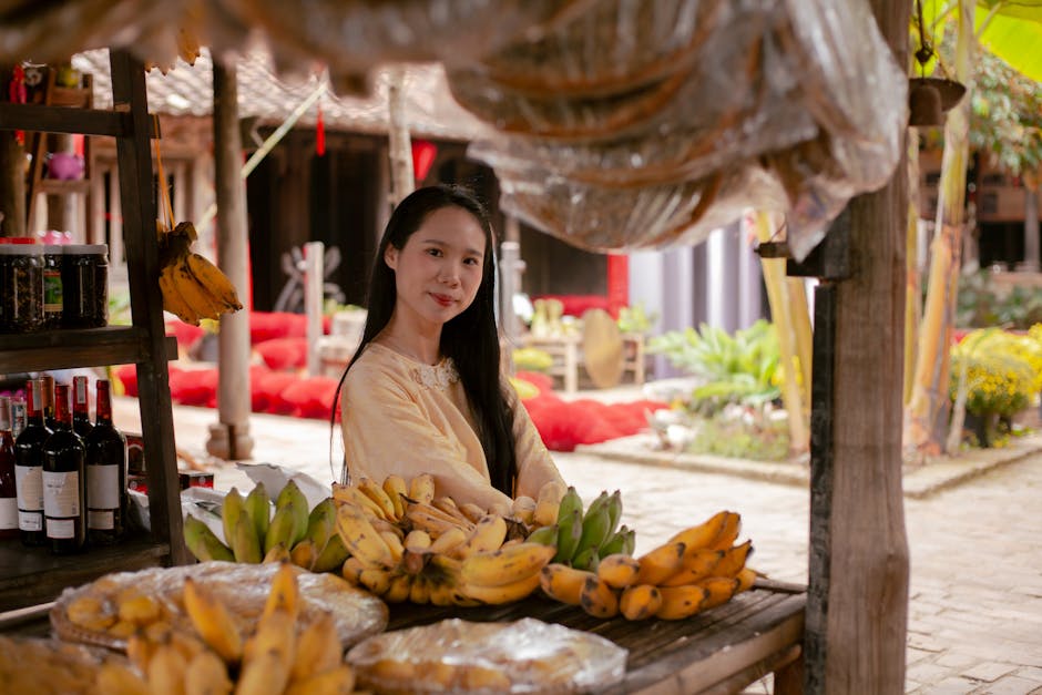 Woman smiling at a rustic outdoor fruit market surrounded by bananas and wine.